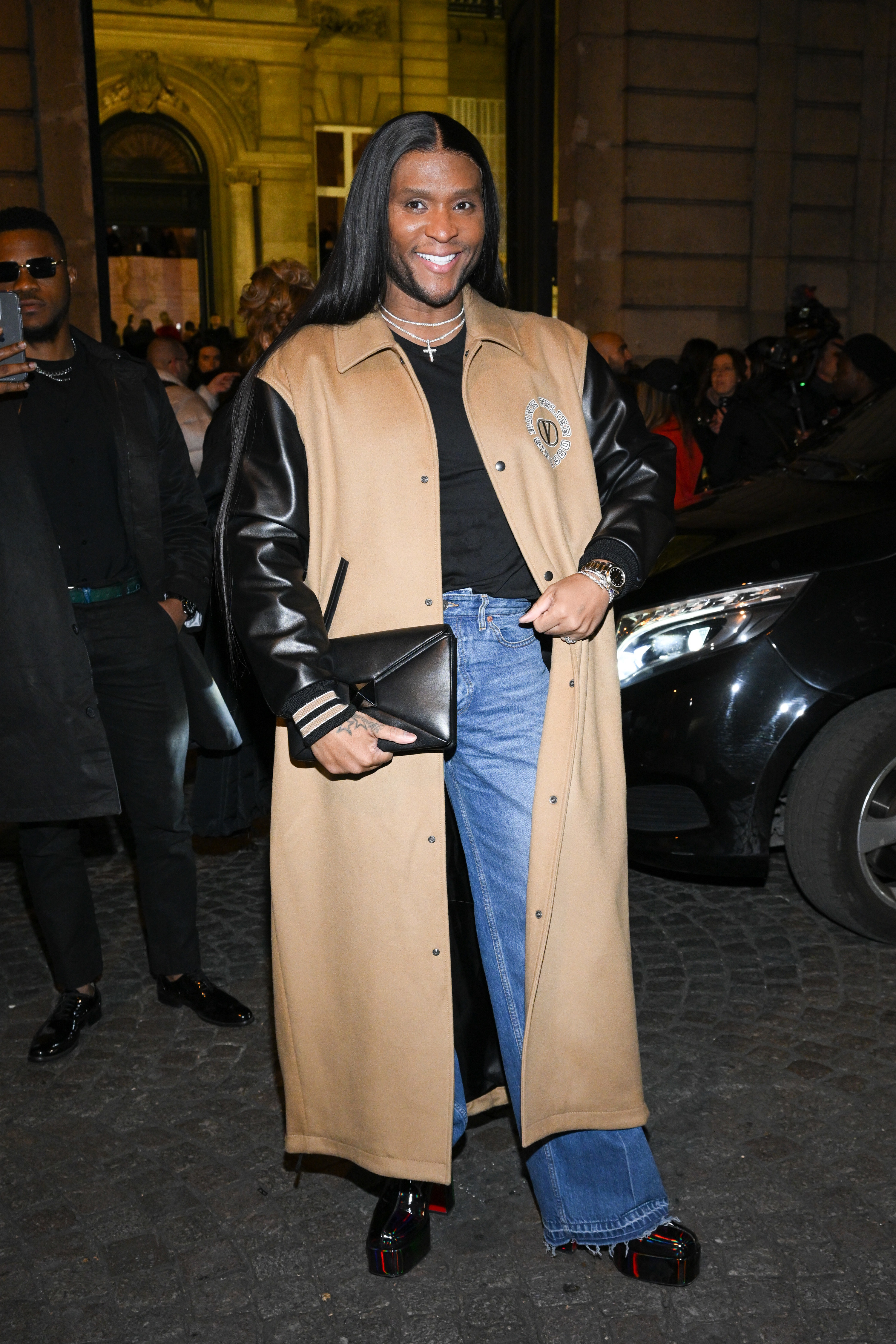 Law smiles as he stands outside at an evening event. He&#x27;s wearing a long coat and jeans