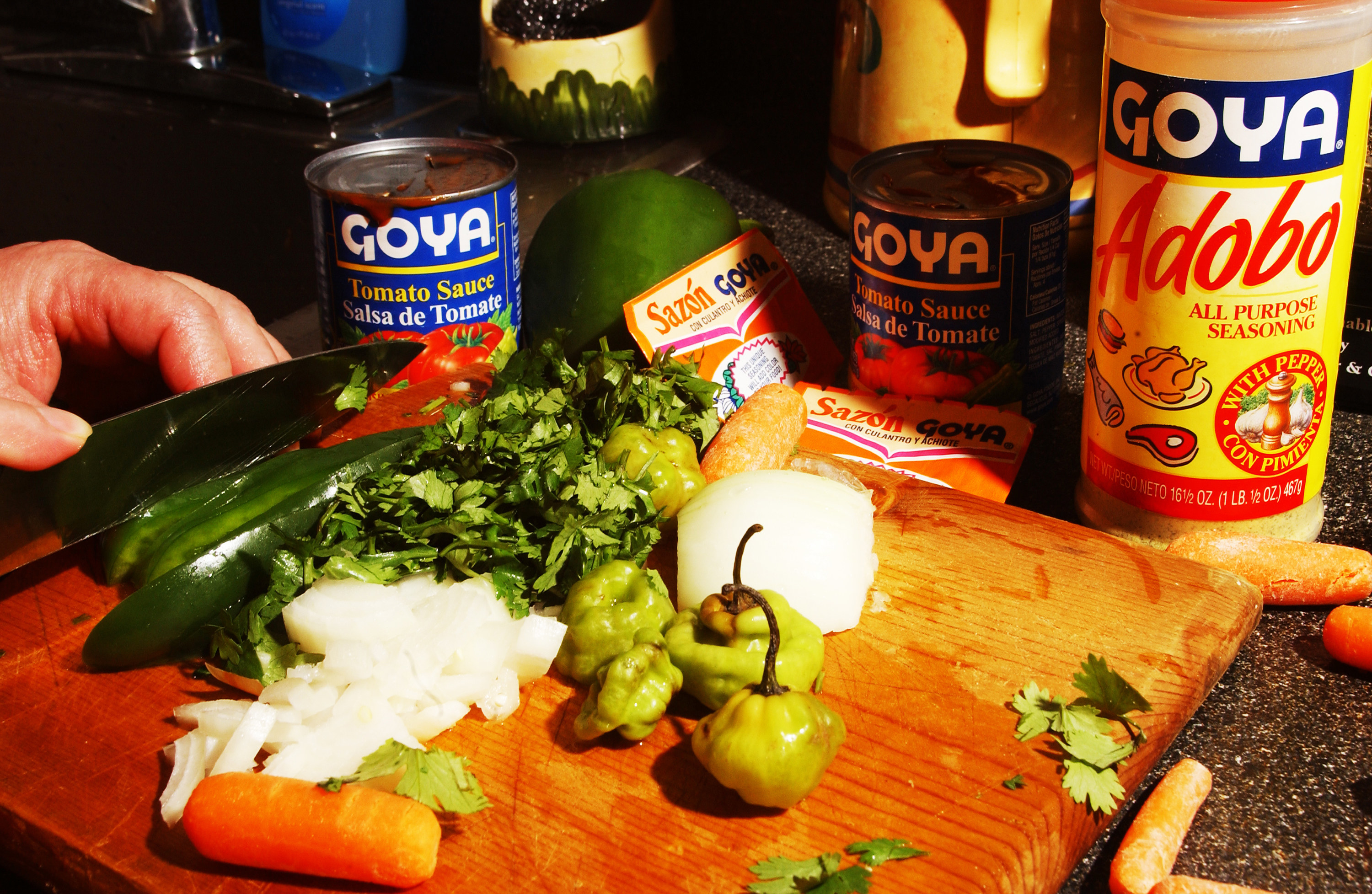 Photo of a knife cutting several vegetables with seasonings in the background