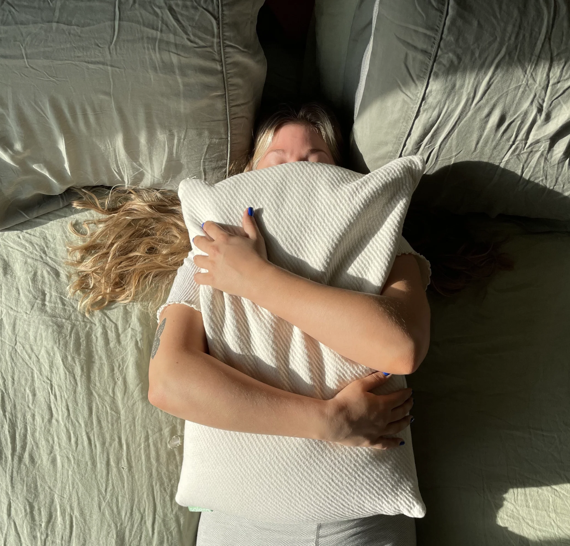 Model laying down on bed hugging Hemp Hull Pillow