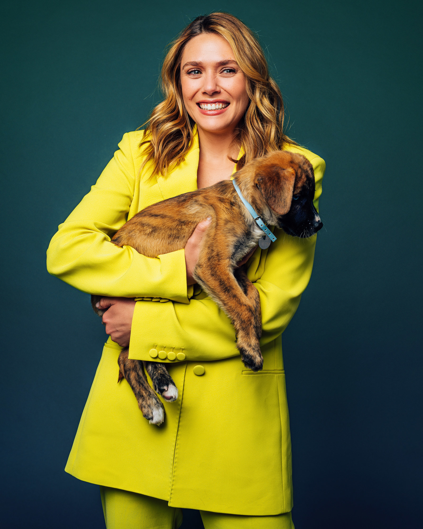 Elizabeth in a yellow suit, laughing, and holding a puppy