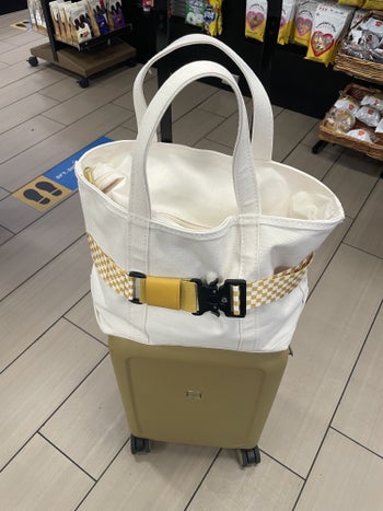 yellow checkered Cincha travel belt holding a tote bag to a BuzzFeeder's suitcase