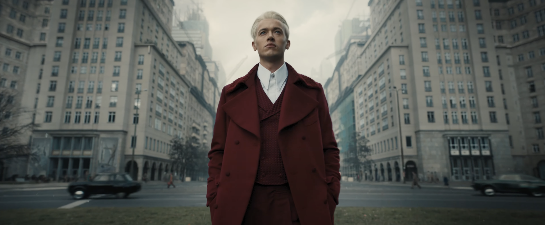 A young man walks through a city in a long coat