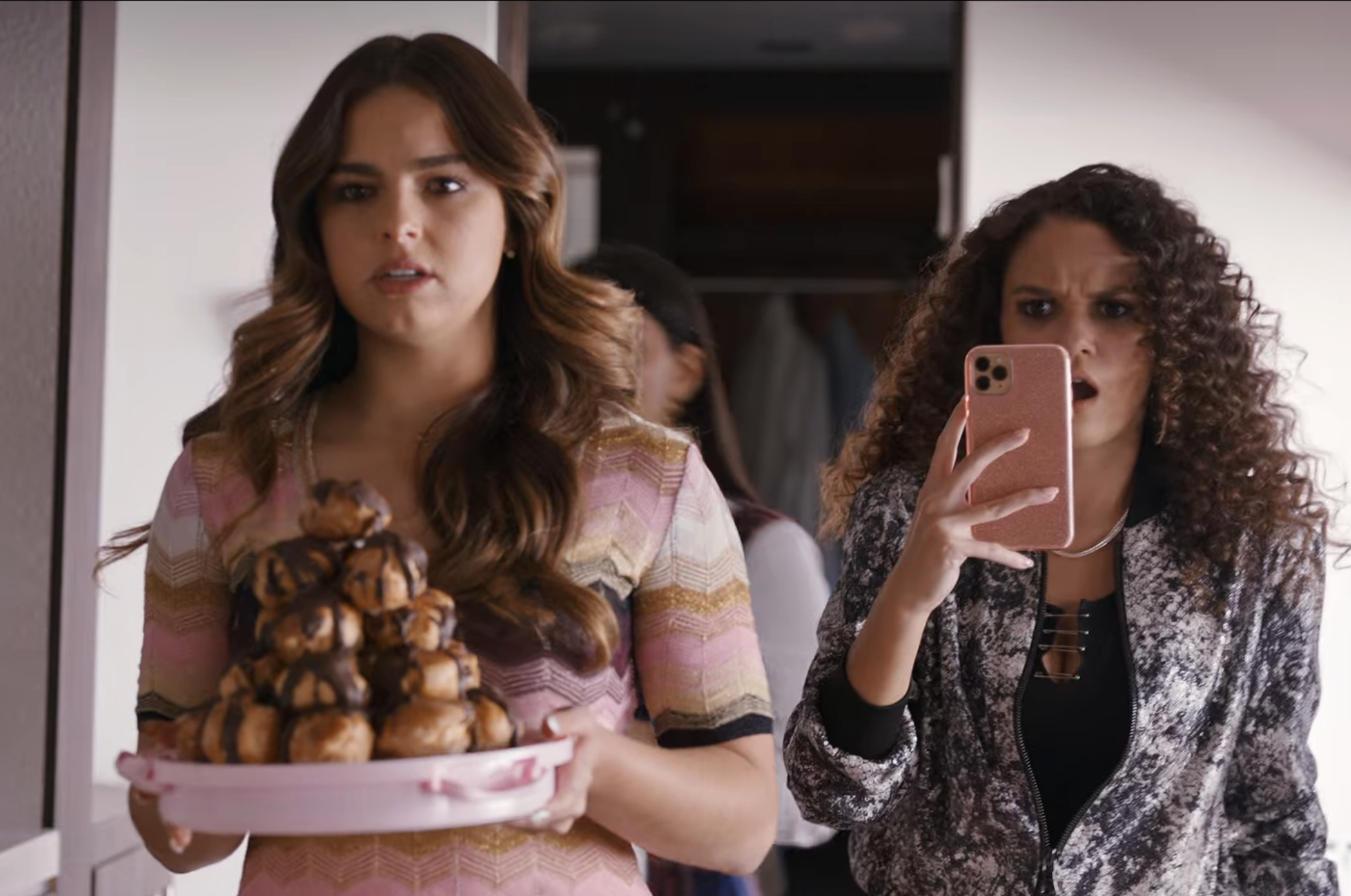one person holding a plate of desserts while someone behind holds up their phone