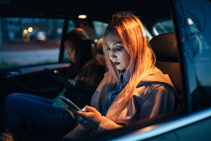 A woman sitting in a car looking at her phone