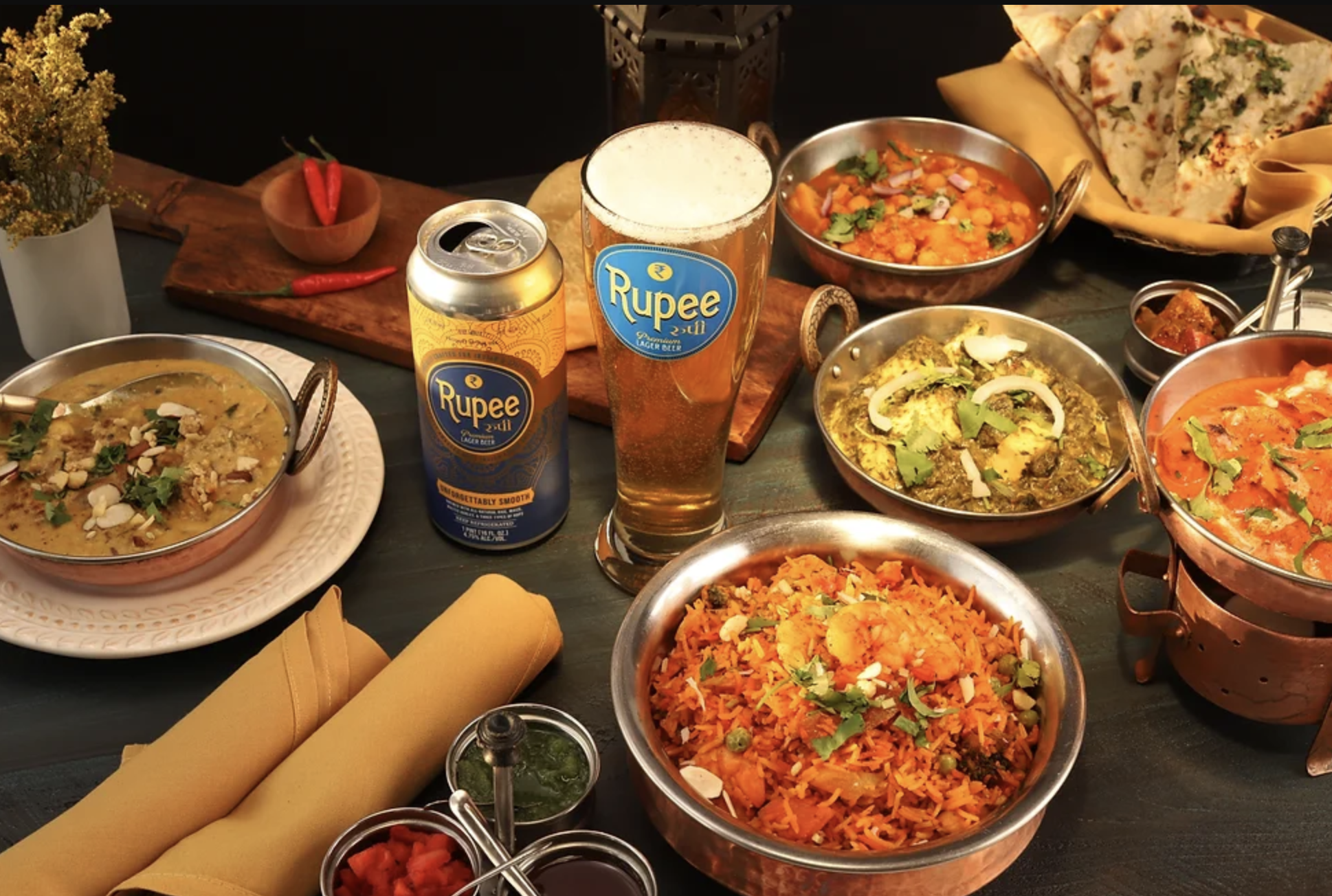 Beer can and cup surrounded by Indian food