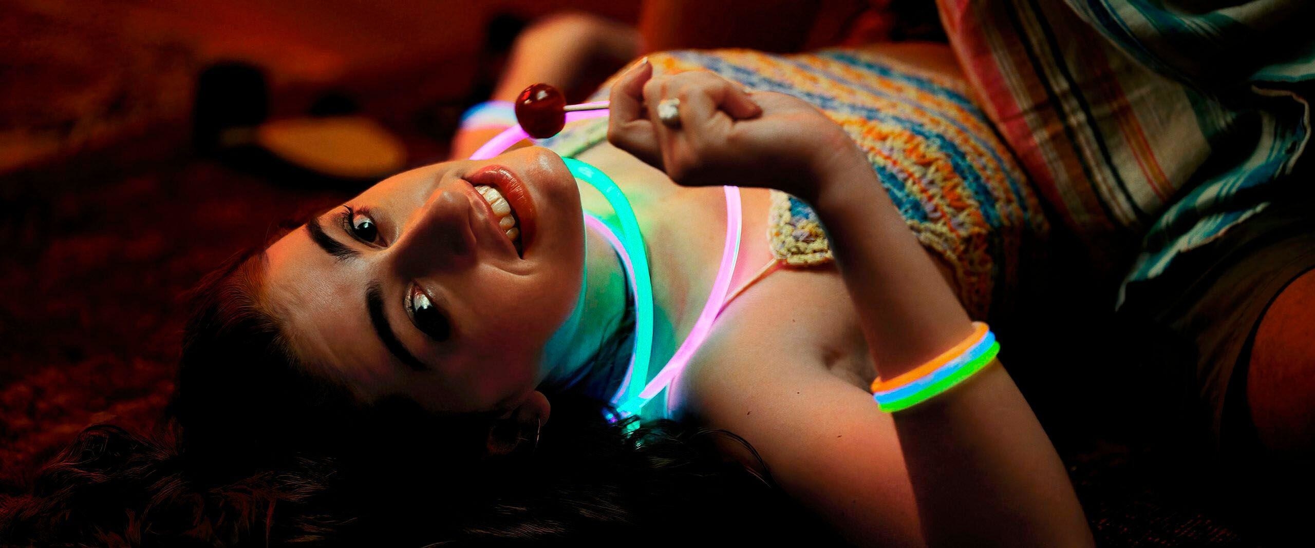 Rachel Sennott lays on a rug with glow sticks and a lollipop