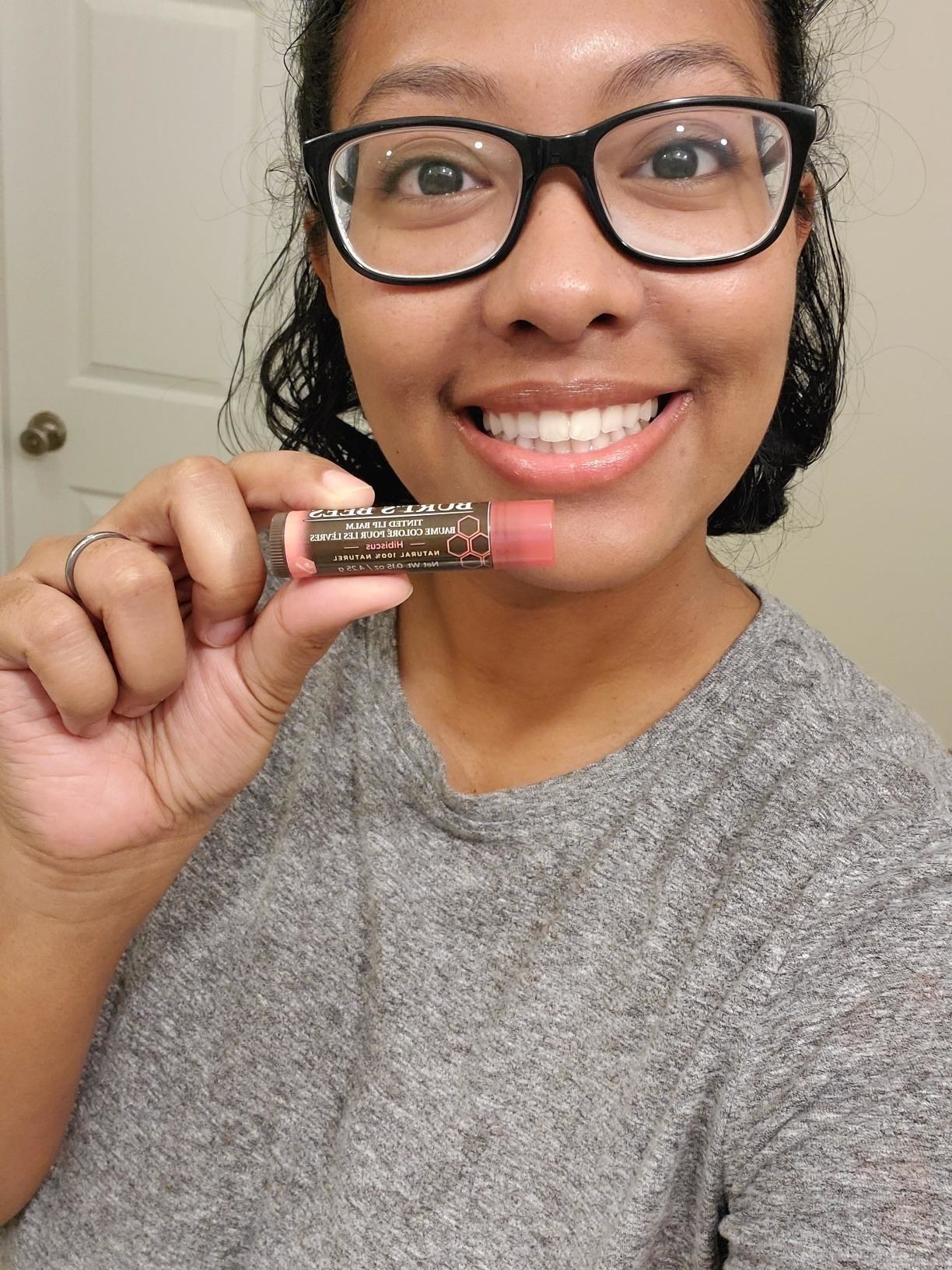 Reviewer wearing the hibiscus balm on lips and holding up balm
