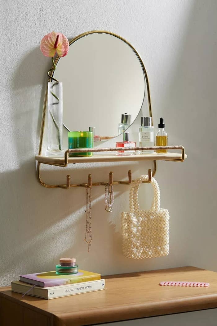 the wall mirror shelf with makeup on it and a purse hanging from the hooks