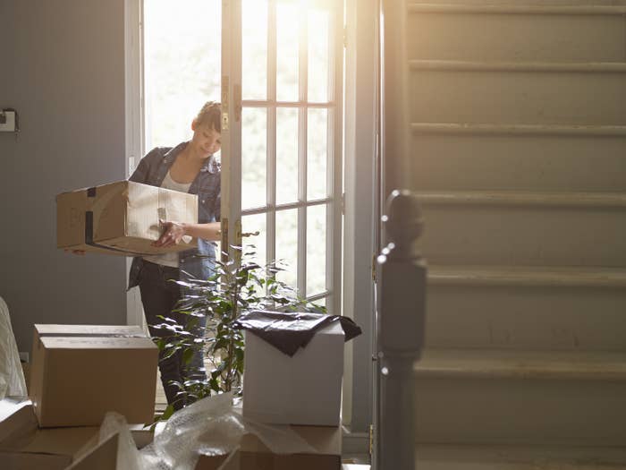 A woman carries a box into her new home