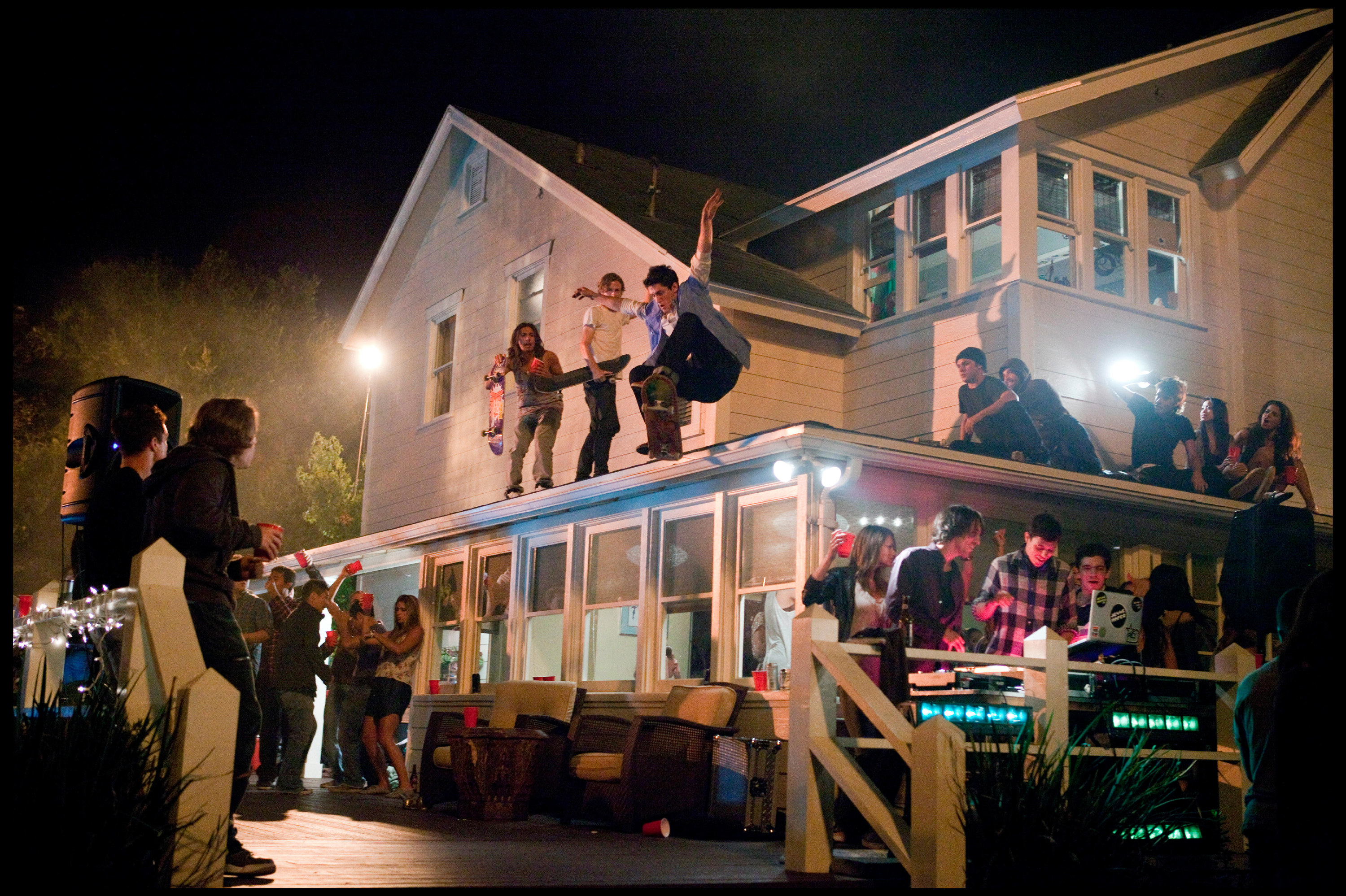 Young skateboarders leap off of a room at a nighttime house party