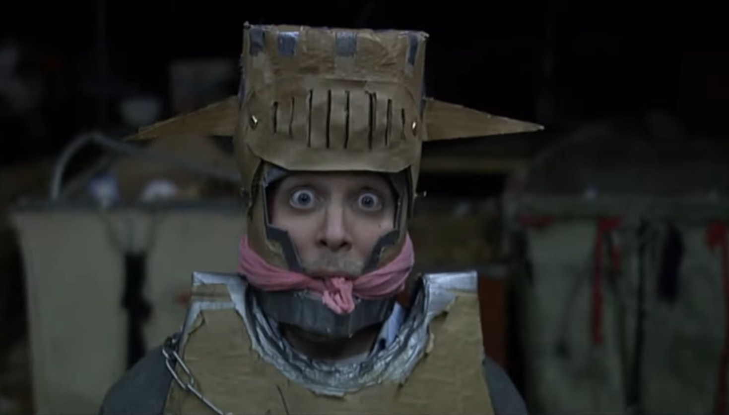 A surprised man in a cardboard Halloween costume is bound and gagged