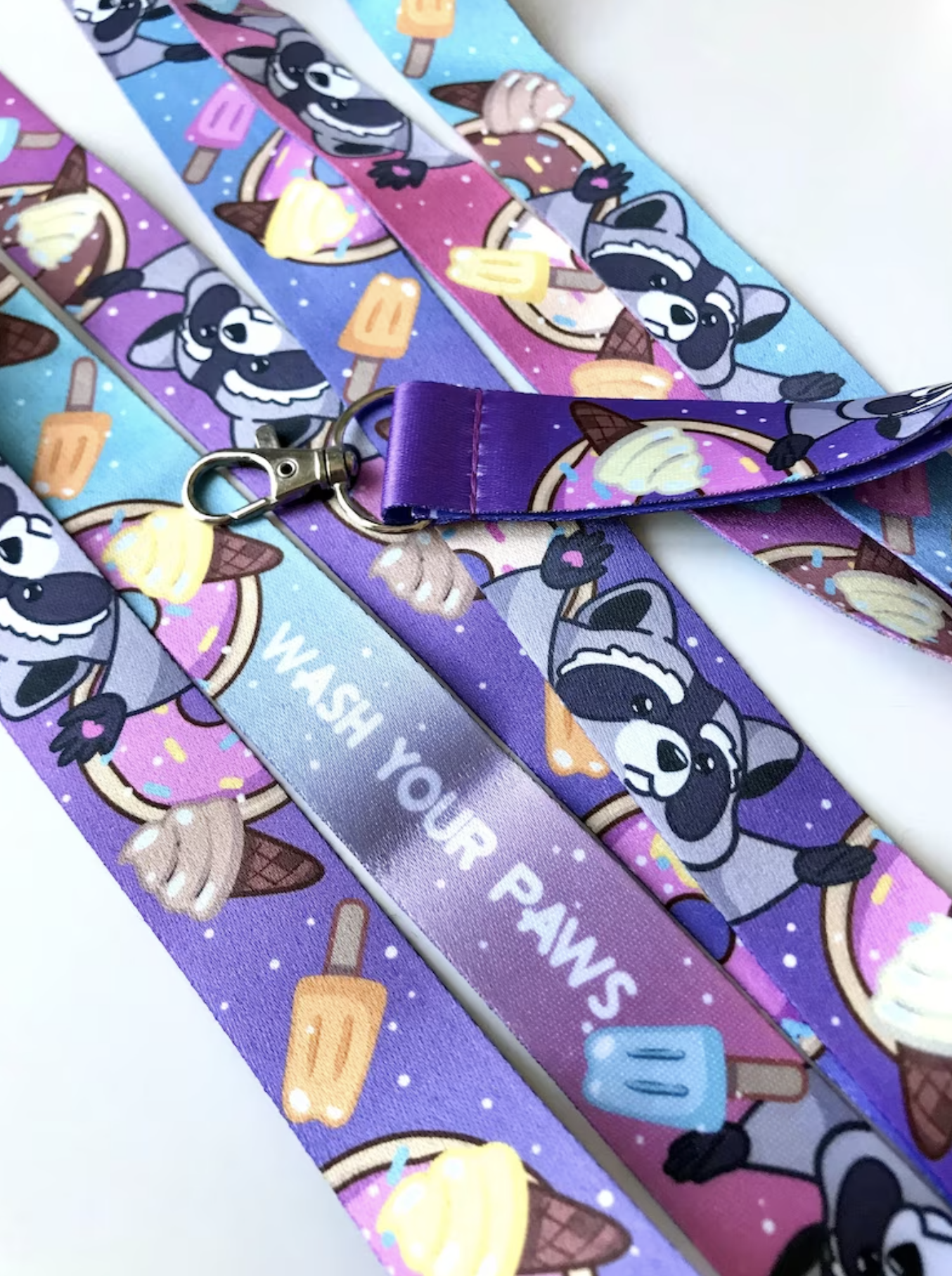 Purple blue and pink lanyard of racoon and food with words "Wash Your Paws"
