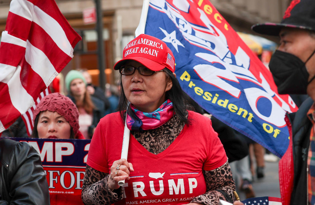 a woman in a ton of prop-trump maga gear stands in a crowd of trump supporters