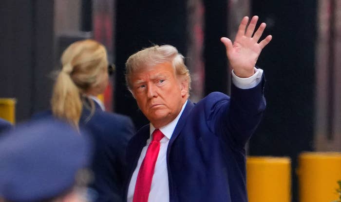 trump in a suit and red tie waving