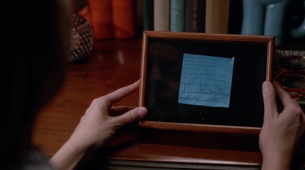 Hands hold a blue Post-It note which has been set in a frame - the Post-It has writing and signatures on it