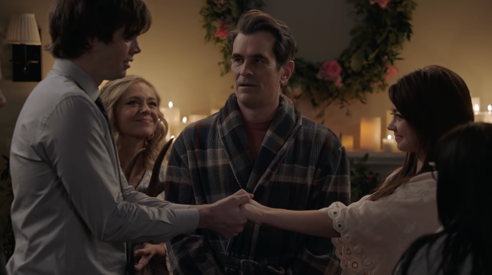 Phil stands in a bathrobe in front of the mantlepiece covered in candles, in front of him Dylan and Haley are standing an arm&#x27;s width apart, facing each other and holding hands