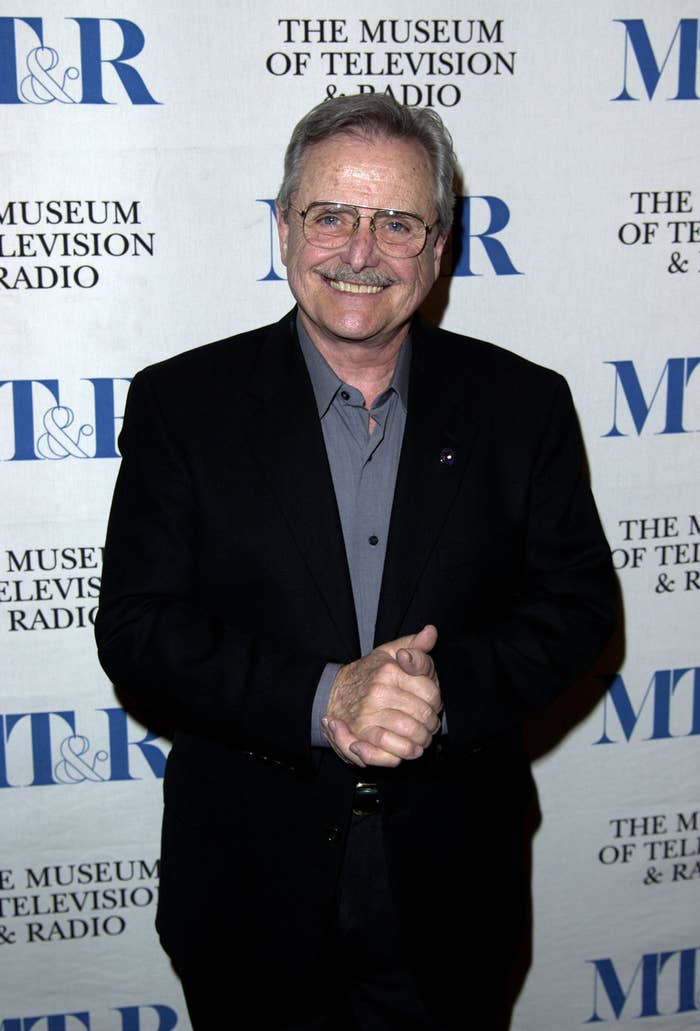 Bill Daniels smiles at a red carpet event. Bill&#x27;s wearing a simple suit and eyeglasses