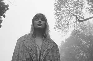 Image of taylor swift from the folklore album cover photoshoot. Grey hues with taylor in an oversized plaid coat looking down at the camera calmly
