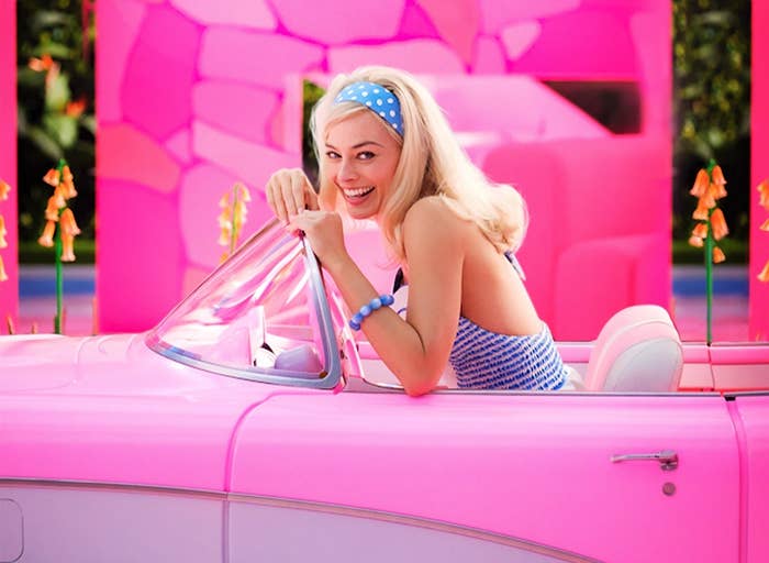 Margot Robbie as Barbie sitting in a pink convertible
