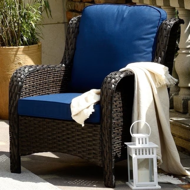 a wicker chair with blue cushioning and a white blanket by a patio
