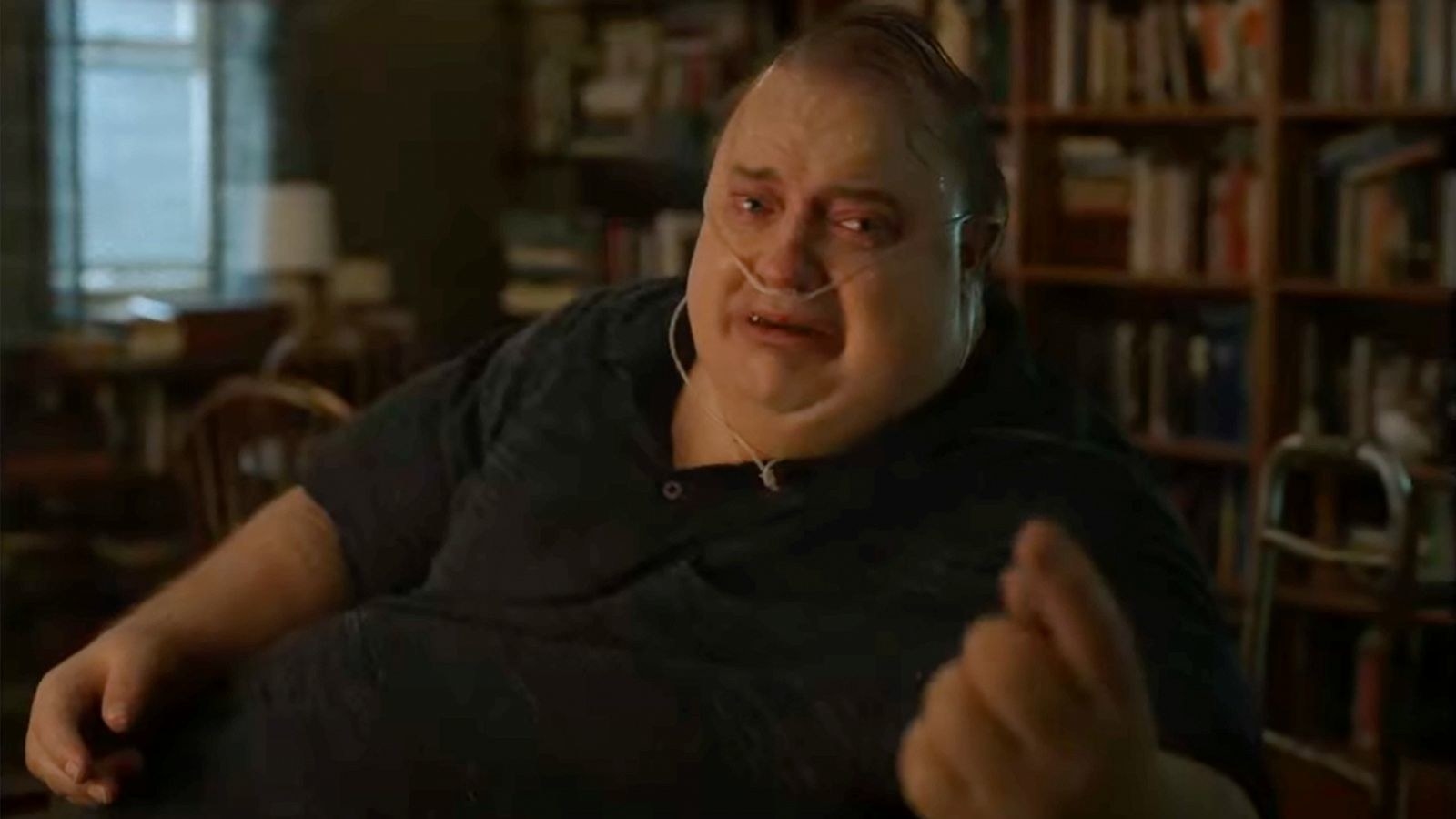 Brendan Fraser in The Whale, his character Charlie sits in a chair with a nasal cannula reaching out to his daughter off screen