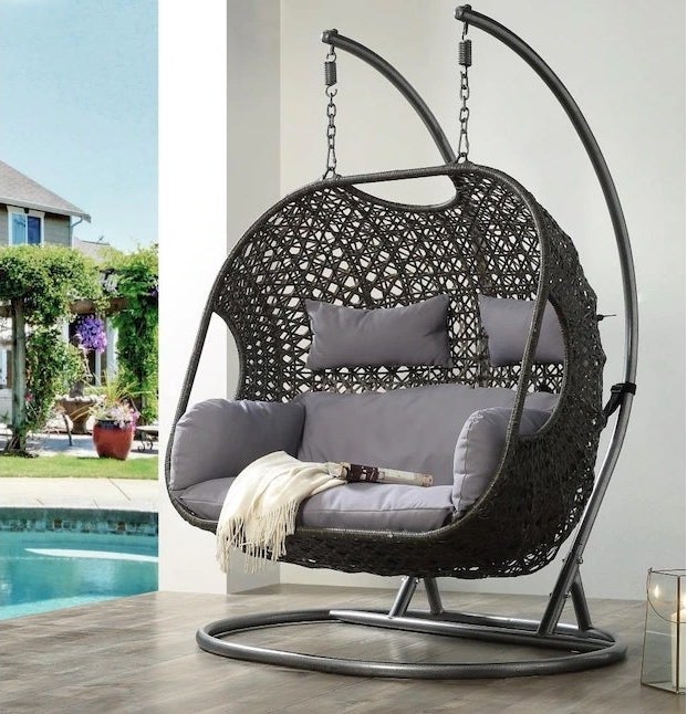 a black hanging chair with gray cushions outside by a pool