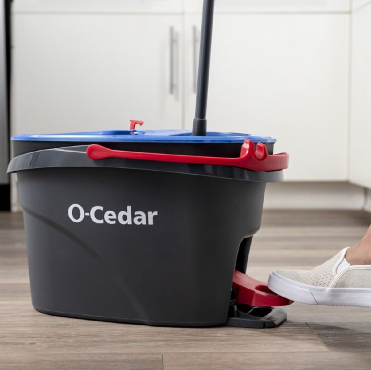 a model using the foot pedal to wring out the mop inside the grey bucket with a red handle