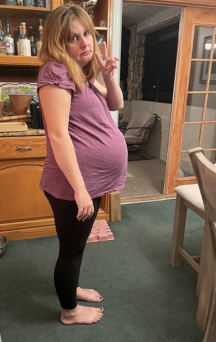 Side view of the very pregnant writer standing and giving a peace sign, looking a bit glum