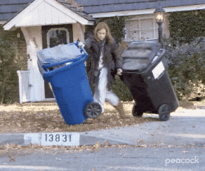 woman dropping her trashcans and picking up the fallen trash by the curb