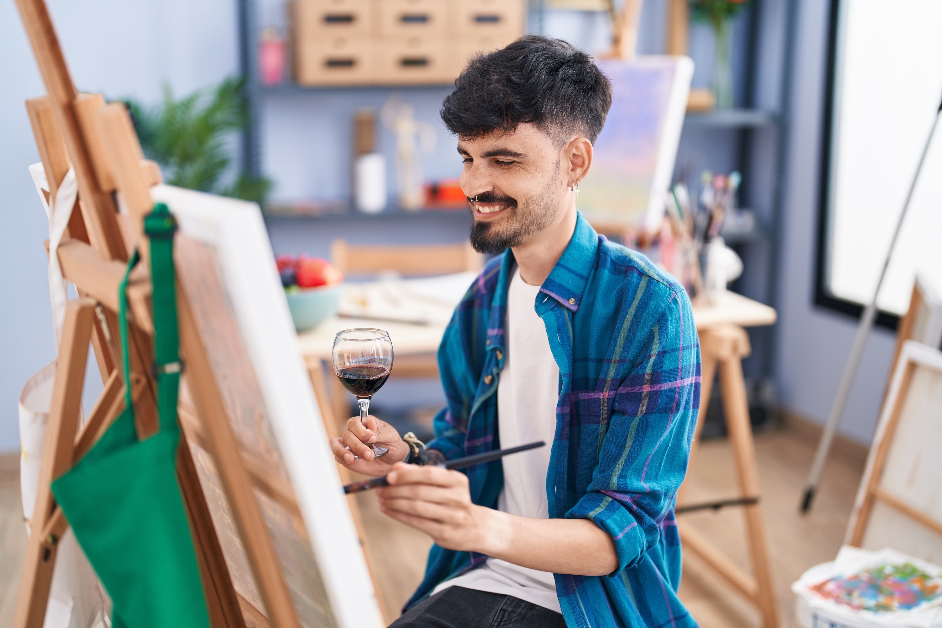 man smiling and painting while holding a glass of wine