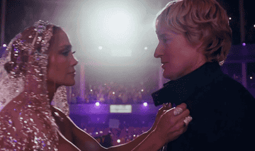 A GIF from Marry Me, Jennifer Lopez wears an ornate veil and she leans in to kiss Owen Wilson in front of a huge stadium crowd