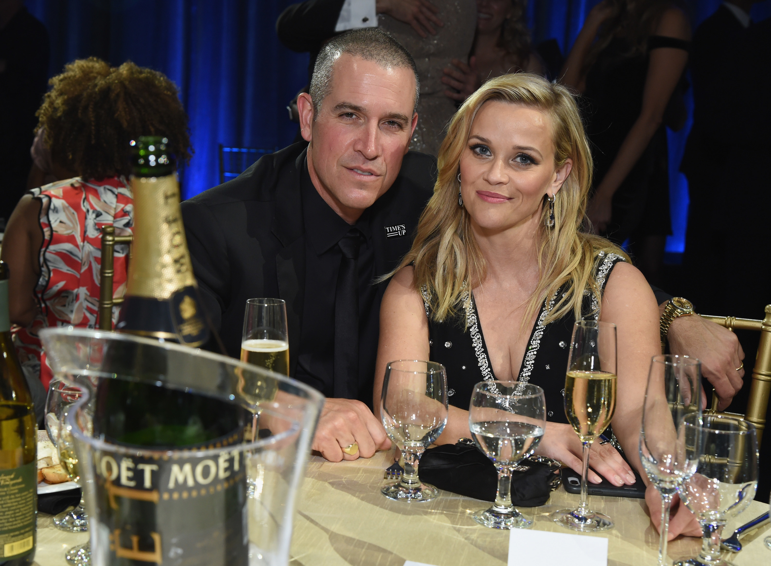 Jim Toth and Reese Witherspoon at an event sitting at a table with champagne and water