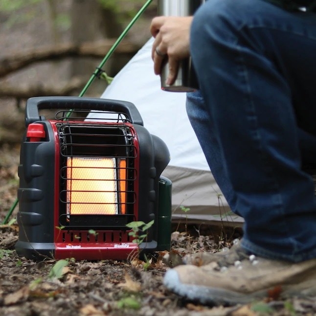a person next to a portable heater in the woods