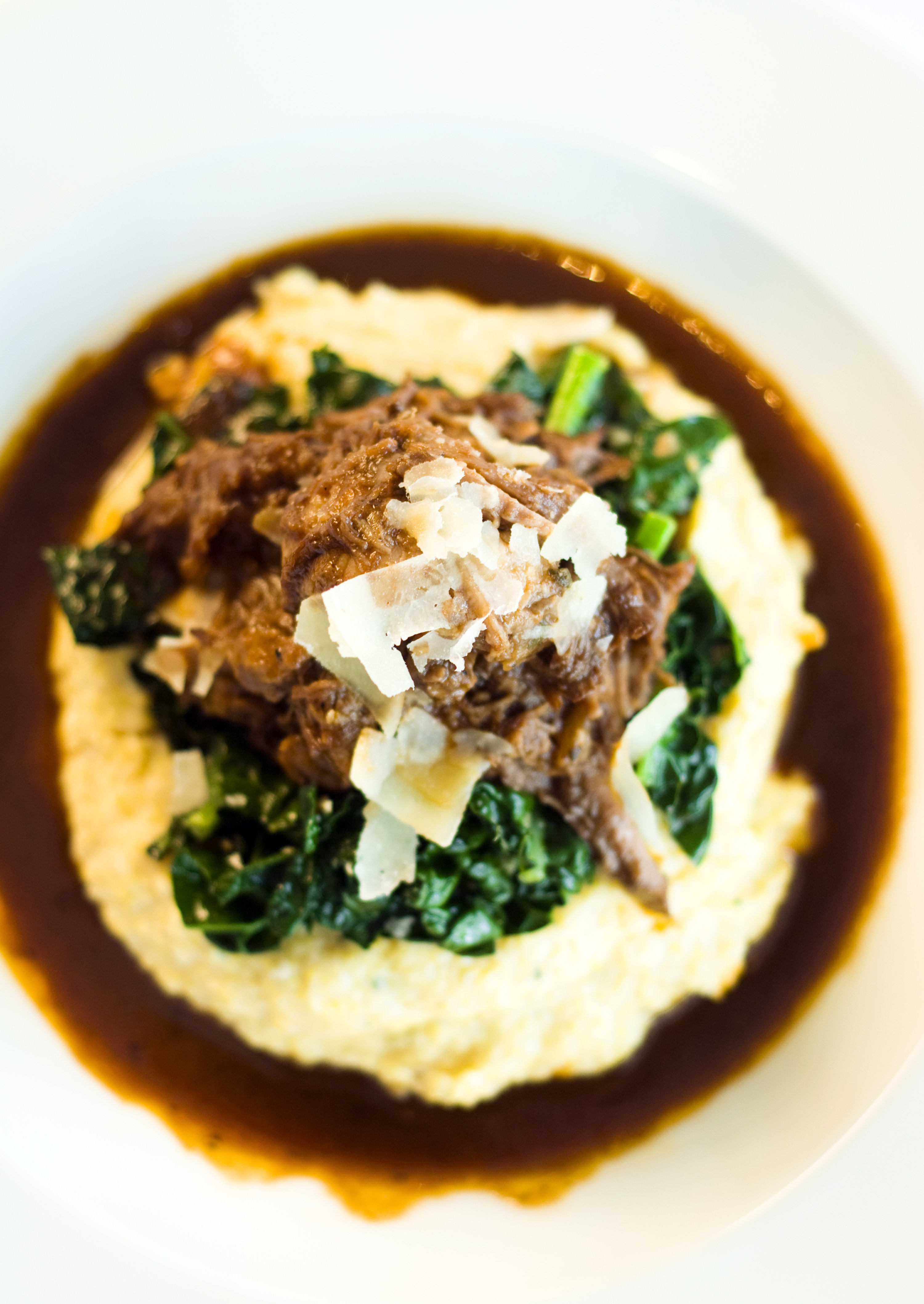 shredded beef over greens and mashed potatoes with a red wine sauce around them