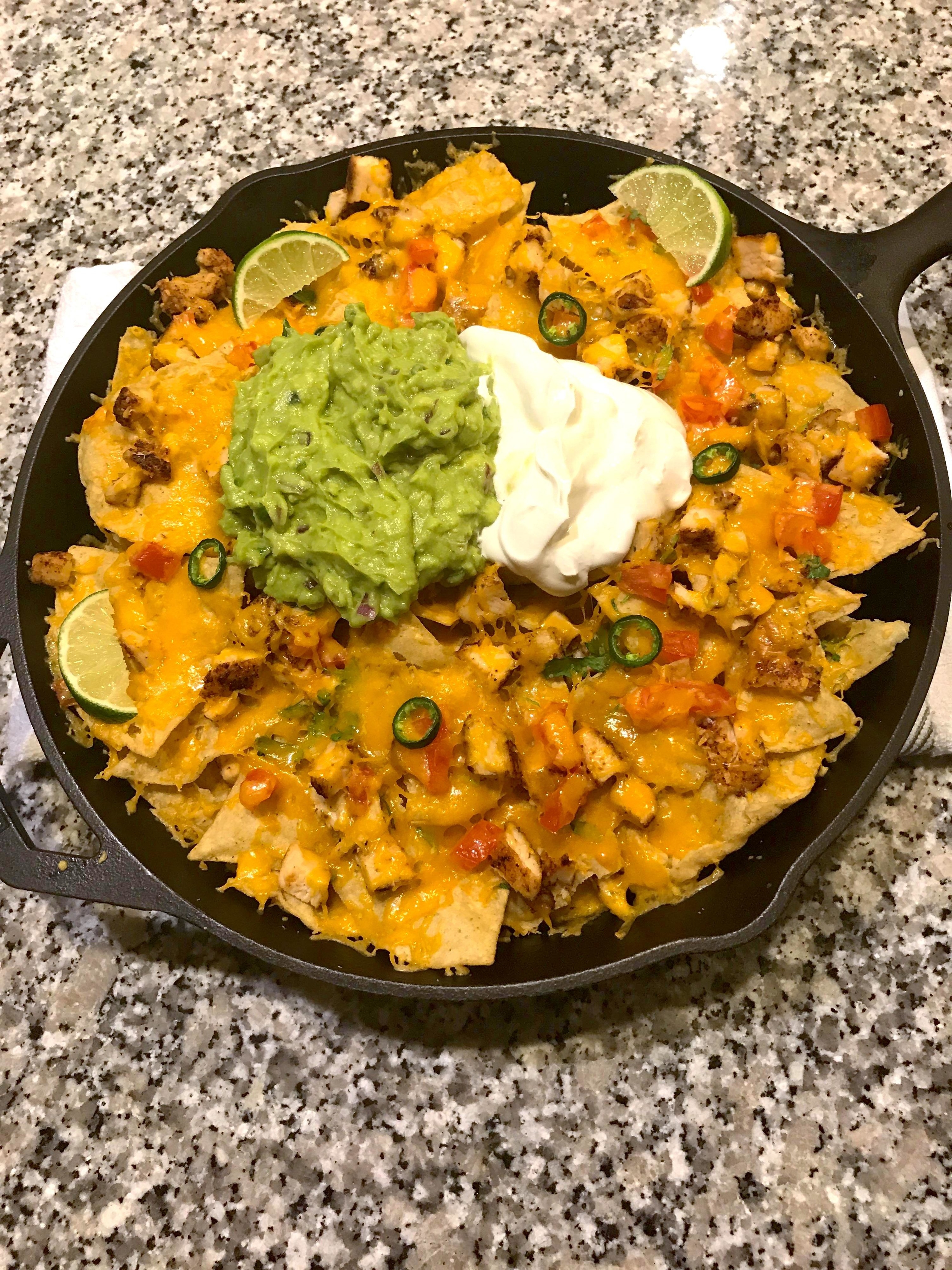 cast iron skillet full of blackened chicken nachos, served with lime wedges, guacamole, and sour cream in the middle