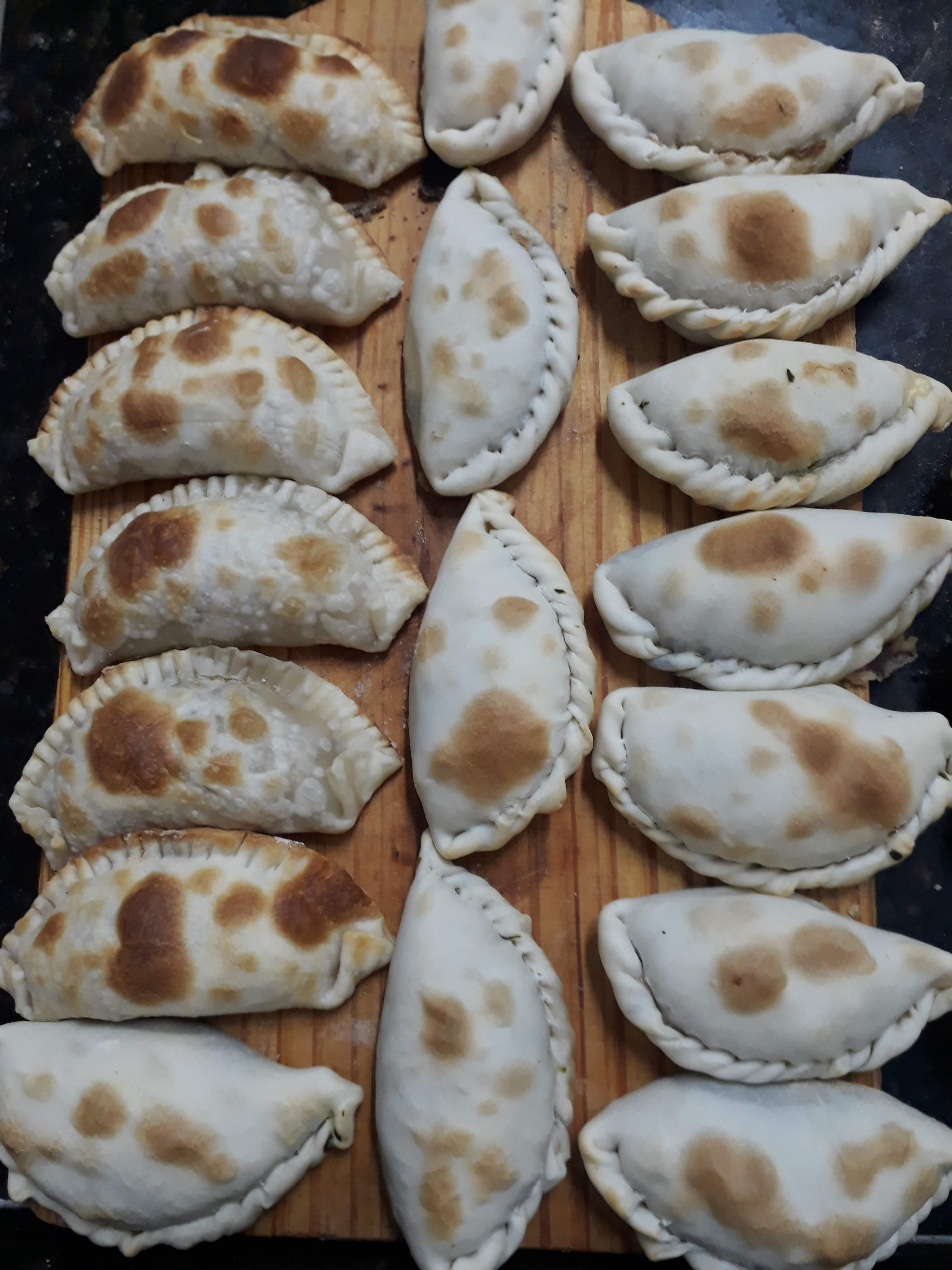 lots of cooked empanadas arranged neatly on a wooden cutting board