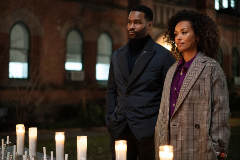 Jabari Reynolds in a suit and turtleneck and Carrie Milgram in a plaid coat standing in front of candles
