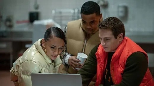 Three friends, including Tariq, looking at a laptop in puffy vests and coats