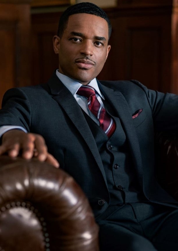 Rashad Tate (Larenz Tate) in a three-piece suit sitting in a leather chair and looking at the camera