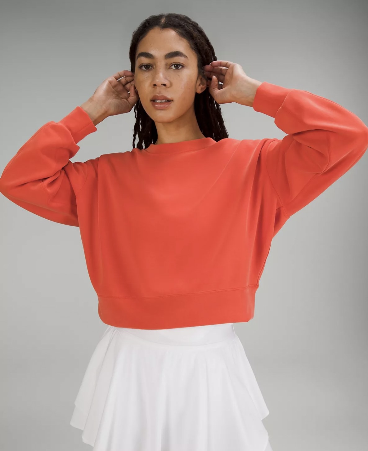 Model with hands up in the orange sweatshirt, paired with white tennis skirt