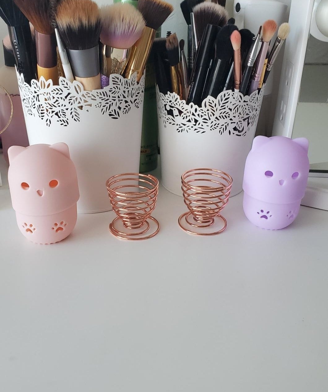 Reviewer&#x27;s pink and purple cat cases and two egg cup-like sponge holders in front of their makeup brush collection