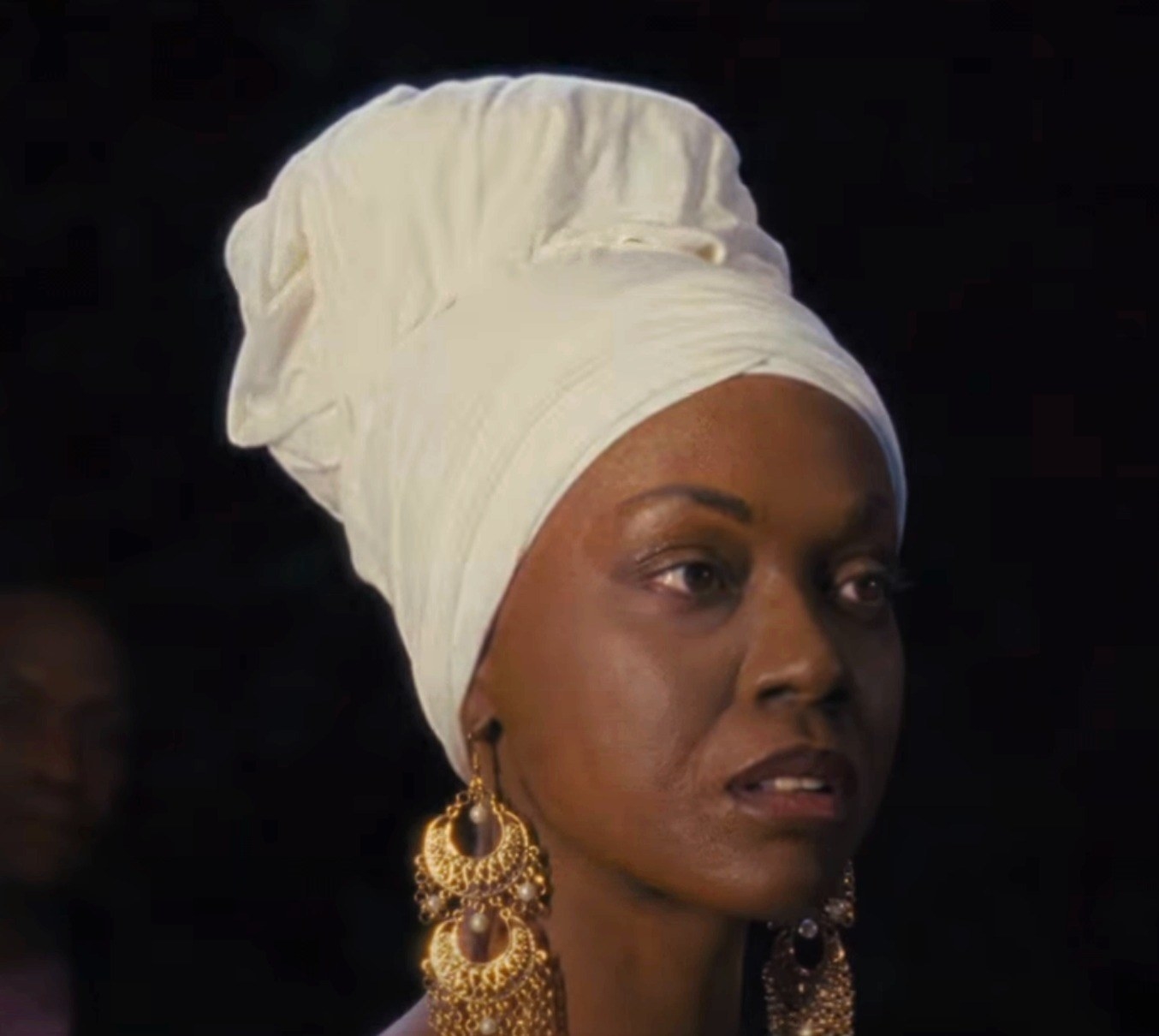 Close-up of Zoe with long earrings, a head wrap, and darkened skin