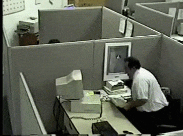 A man hitting his computer monitor off his desk with his keyboard