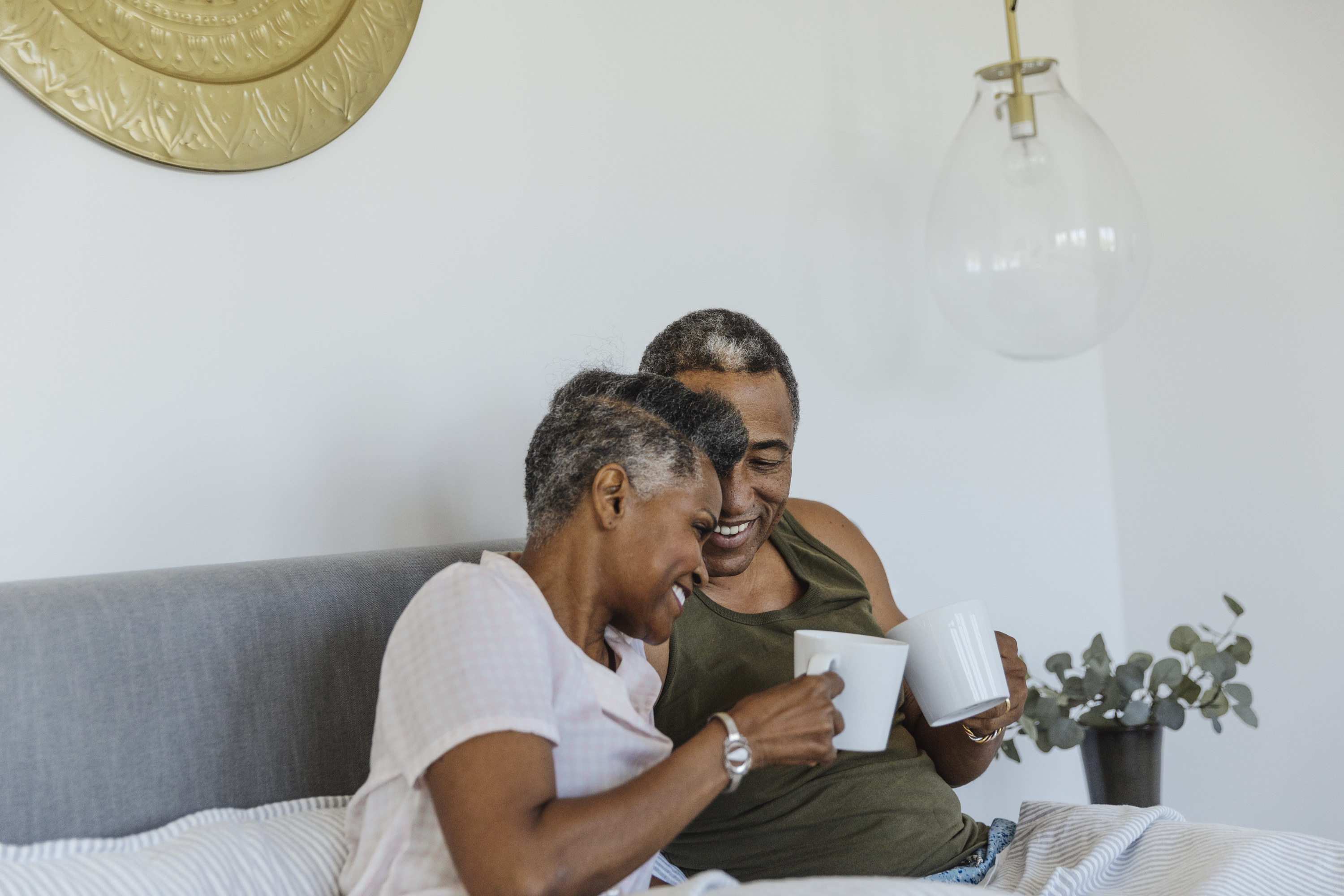 A couple in bed flirting and drinking from mugs