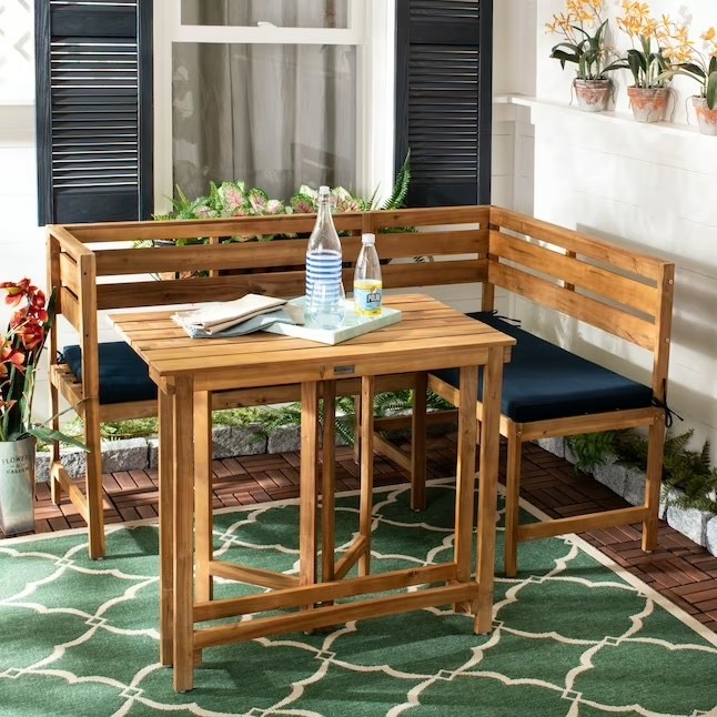 a wood and navy patio set holding beverages and a tray while on top of a green rug and around plants