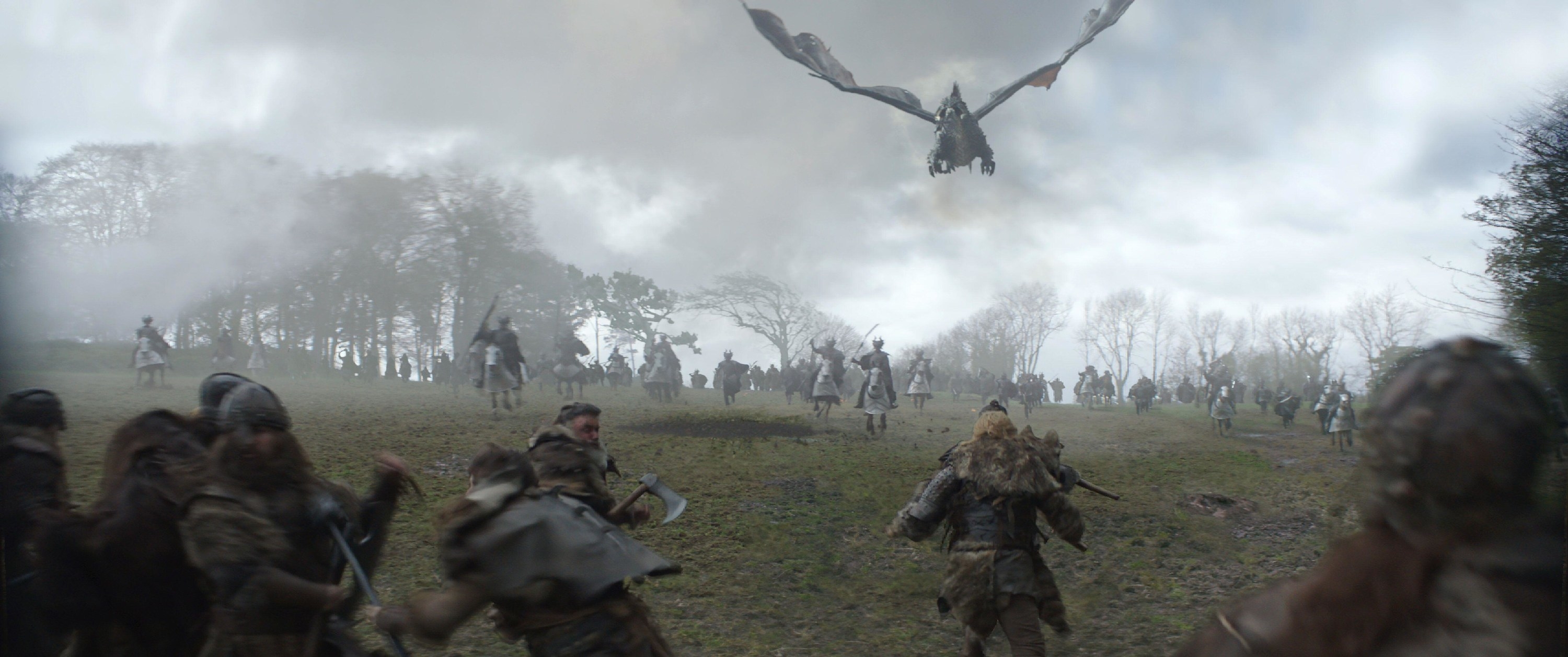A medieval war breaks out on a muddy battlefield with a dragon flying overhead