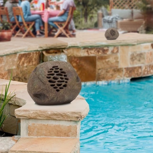 two bluetooth speakers resembling rocks and placed by a pool