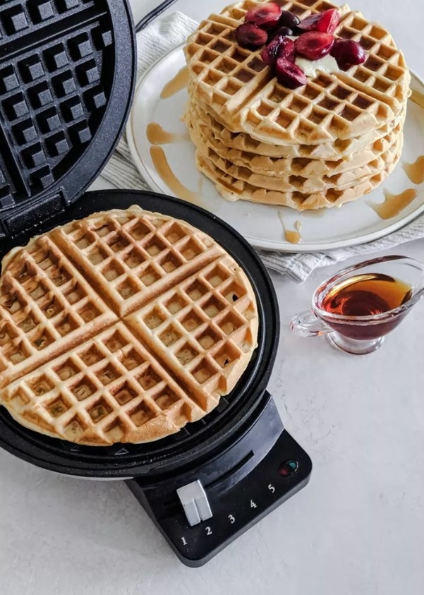 The waffle maker cooking a waffle on setting 2 with a stack of waffles on a plate beside it