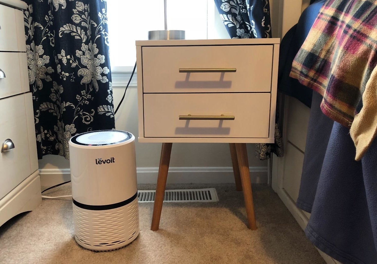 A reviewer's photo of a white air purifier with black accents and a blue light