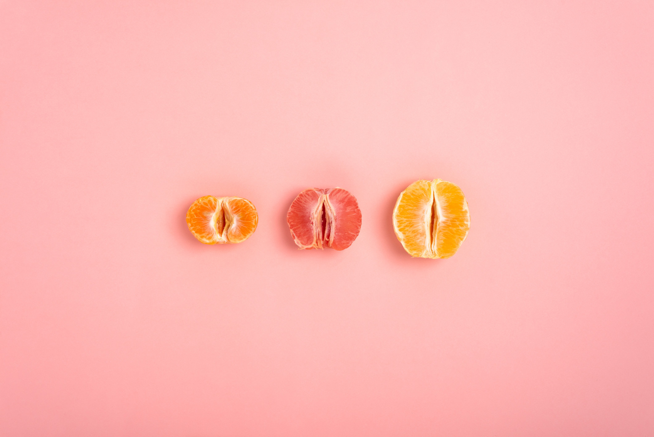 tangerine, grapefruit and orange cut in half on a peach background